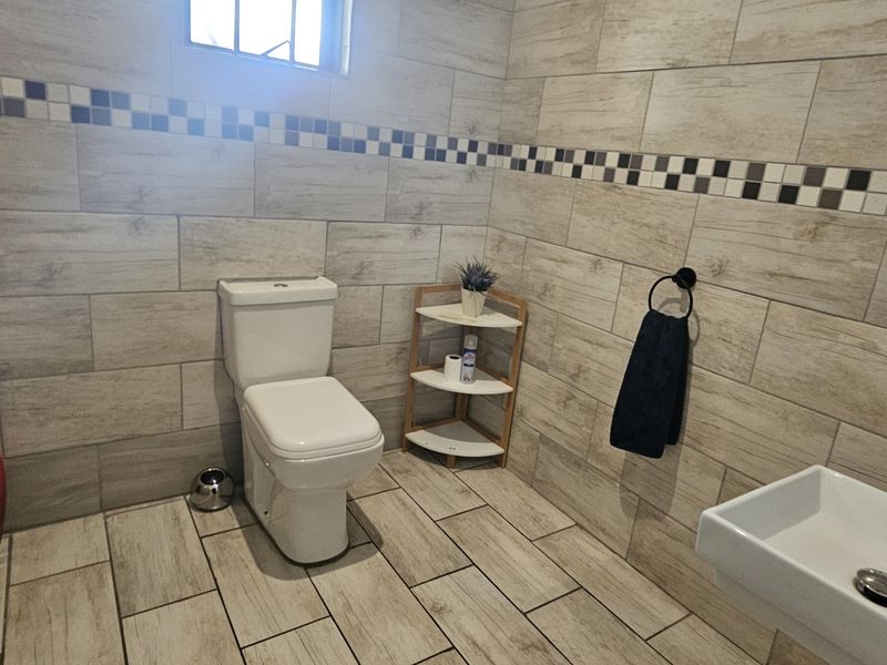 A modern bathroom featuring wood-look tiled walls with a decorative border, a white toilet, and a wall-mounted basin.