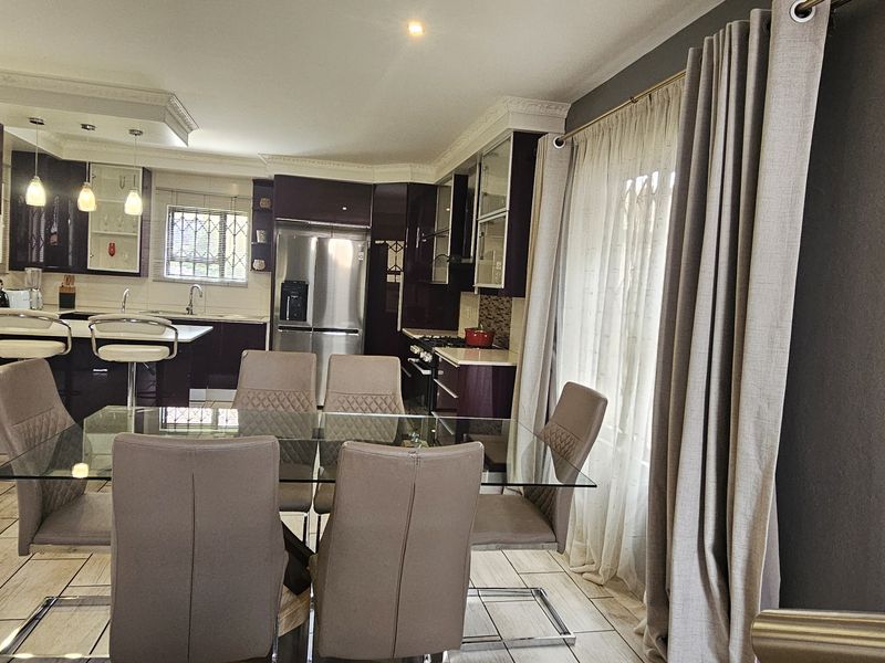 An open-plan kitchen and dining area featuring dark cabinetry, a central island with breakfast bar seating, and modern tiled flooring.