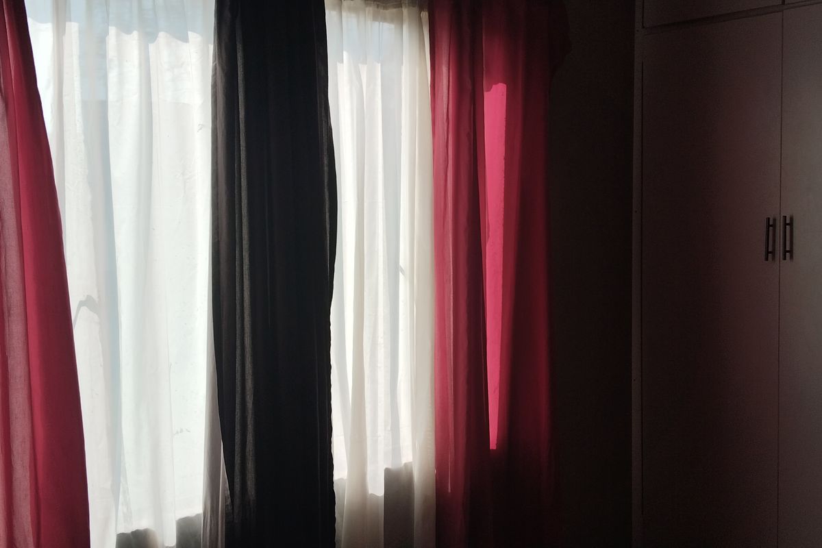 A bedroom interior featuring a built-in wardrobe and window with layered curtains, providing natural light and storage space.