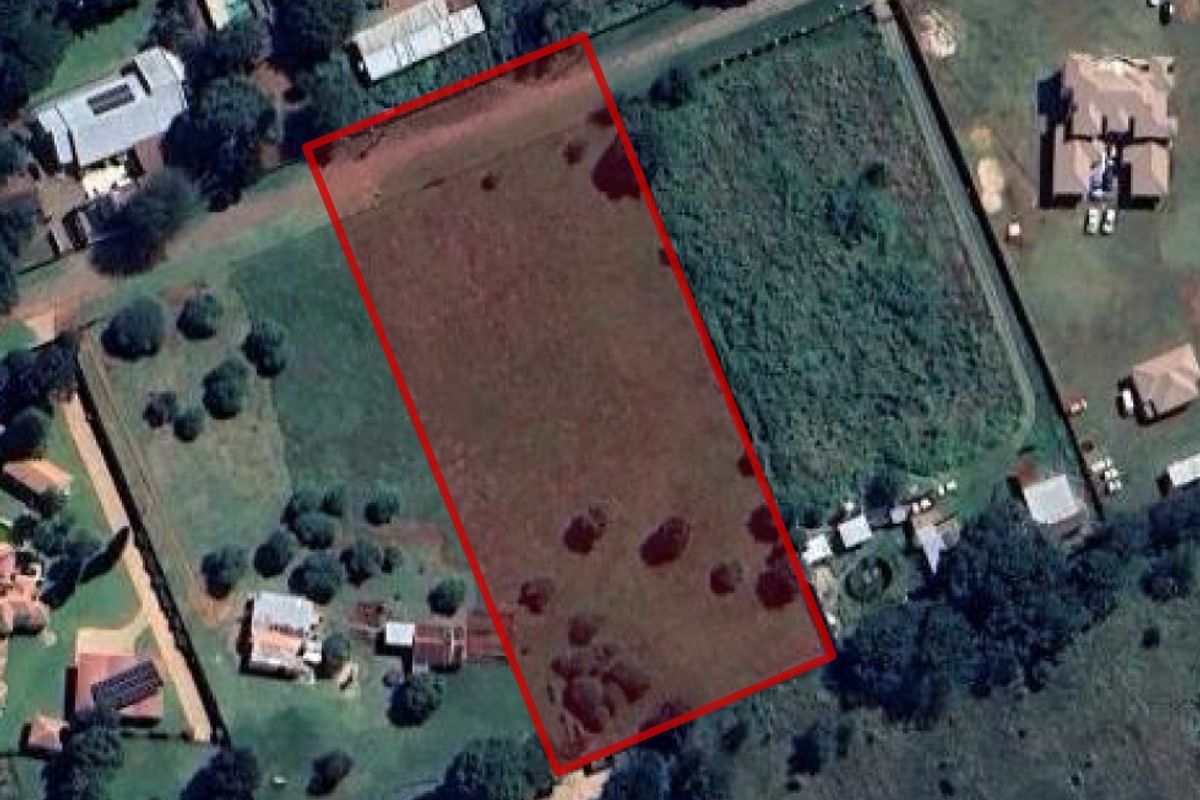 An aerial view of a vacant residential plot outlined in red, situated within an established neighborhood.