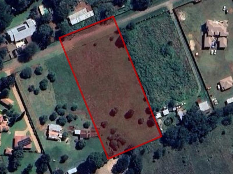 An aerial view of a vacant residential plot outlined in red, situated within an established neighborhood.