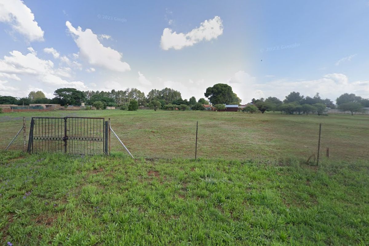 A view of a vacant residential plot featuring a metal gate and wire fencing, offering a clear perspective of the open land.