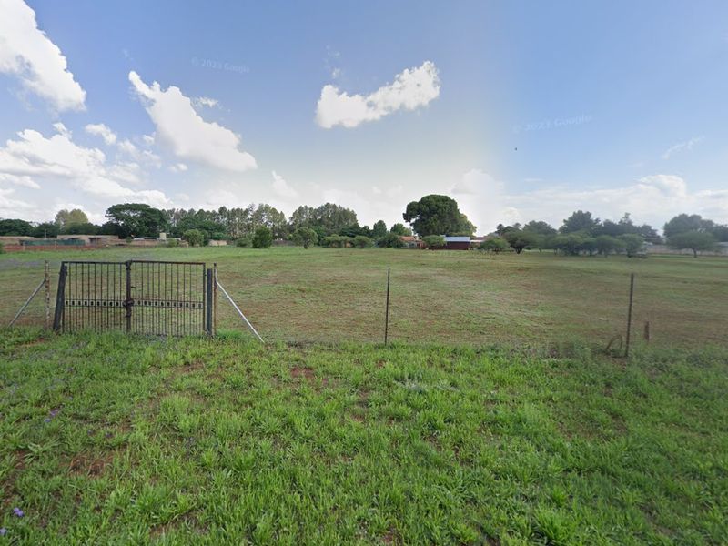 A view of a vacant residential plot featuring a metal gate and wire fencing, offering a clear perspective of the open land.