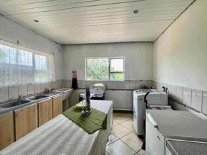 A functional laundry room featuring built-in cabinetry, a double sink, tiled flooring, and a tiled splashback, offering ample space for utility appliances.
