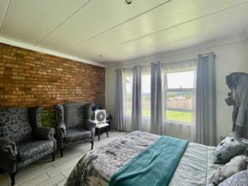 A bedroom featuring an exposed brick wall, tiled flooring, and large windows that provide natural light.