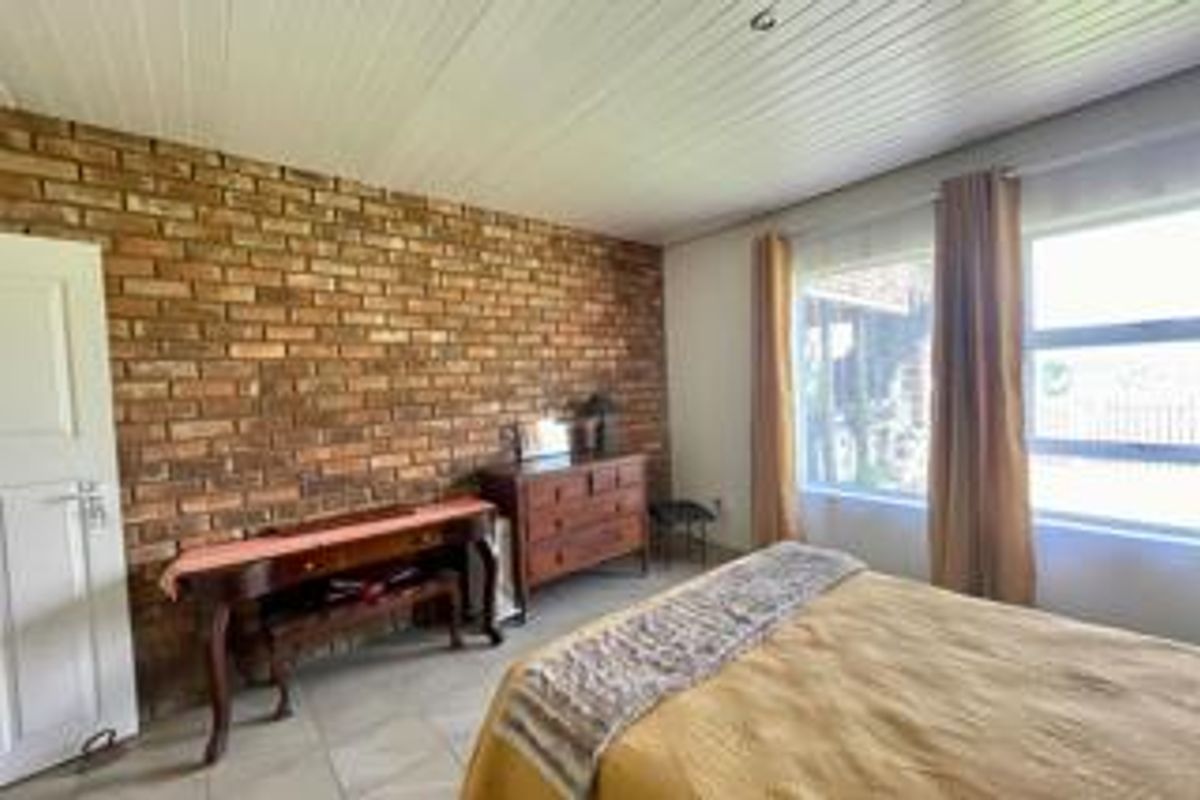 A bedroom featuring an exposed brick feature wall, timber panelled ceiling, and tiled flooring, offering a rustic aesthetic with natural light.