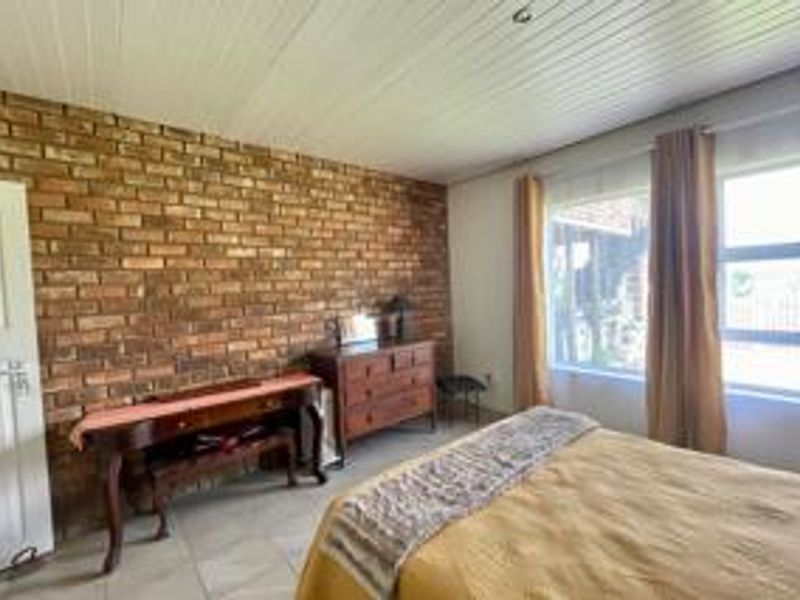 A bedroom featuring an exposed brick feature wall, timber panelled ceiling, and tiled flooring, offering a rustic aesthetic with natural light.