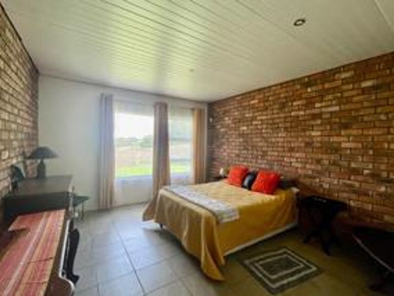 A spacious bedroom featuring exposed brick feature walls, tiled flooring, and large windows that provide natural light.