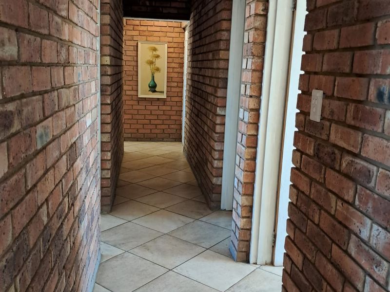 A well-maintained hallway featuring exposed brick walls and neutral ceramic floor tiles, providing a rustic aesthetic and access to multiple rooms.