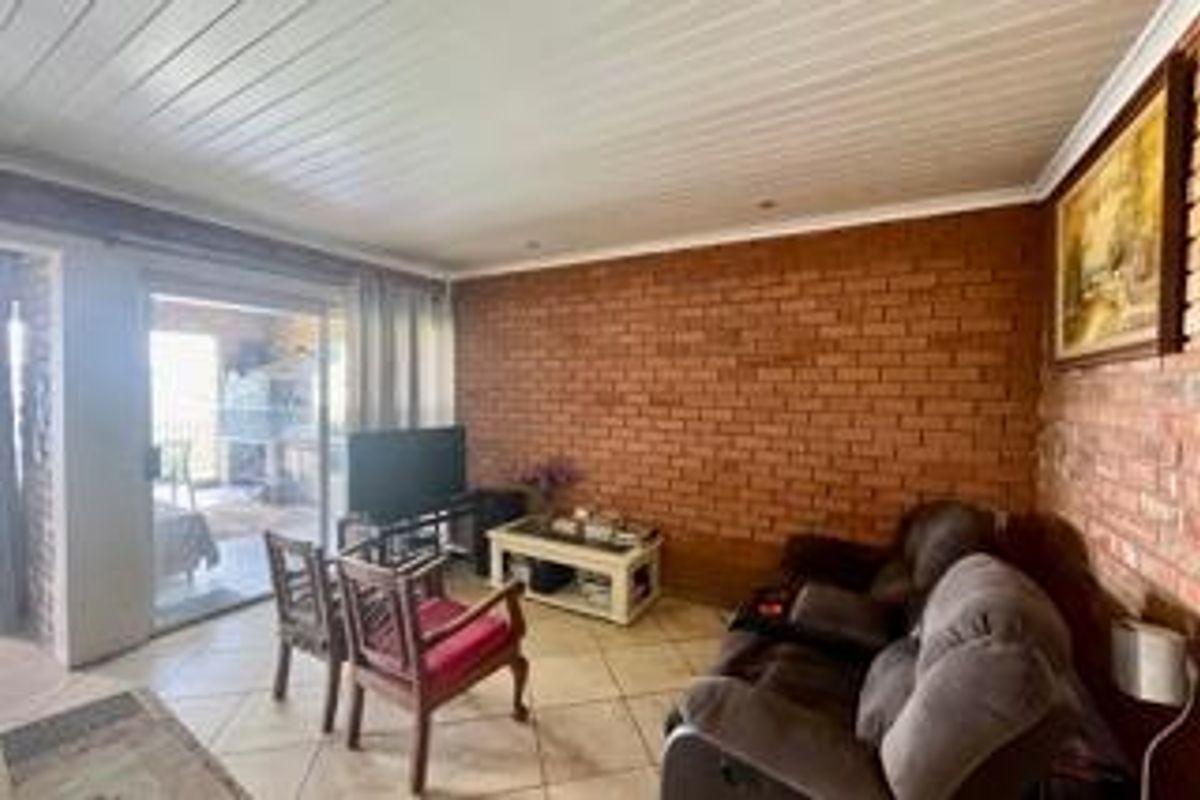 Living room featuring an exposed brick feature wall, timber panelled ceiling, and tiled flooring with direct access to an outdoor patio area.