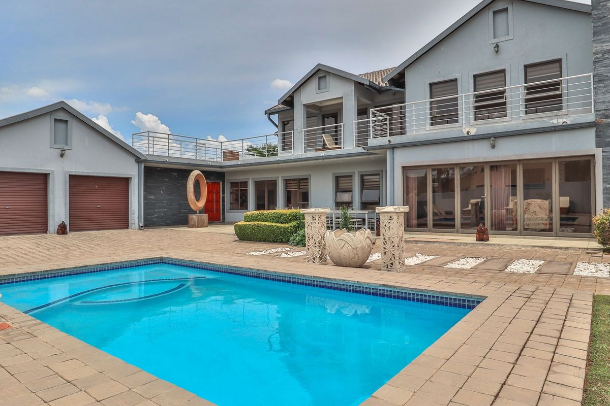 Spacious rear exterior featuring a swimming pool, paved patio area, double garage, and a multi-level home with balcony access and large sliding glass doors.