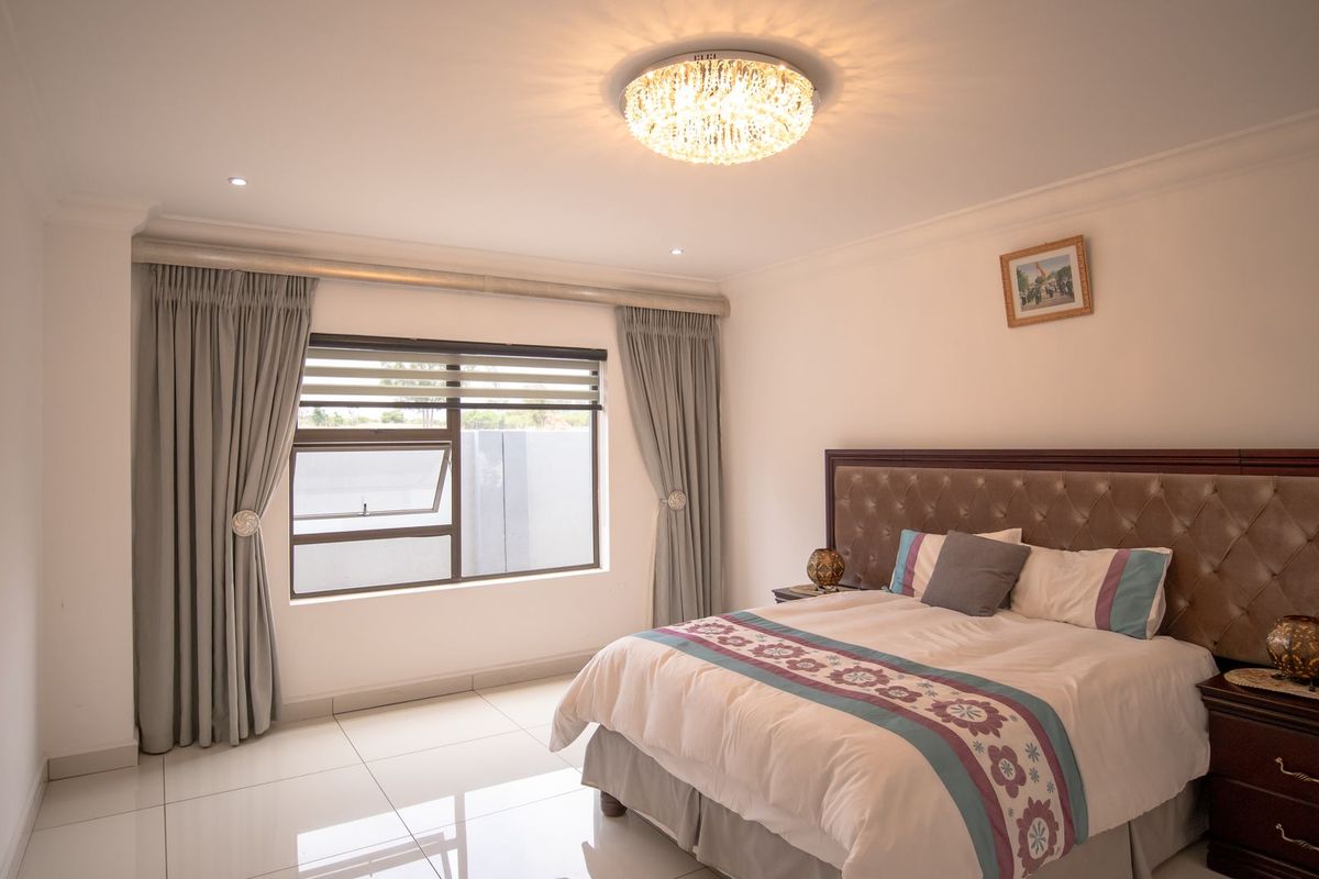 A well-maintained bedroom featuring polished tiled flooring, modern recessed lighting, a decorative crystal ceiling fixture, and large windows with integrated blinds.