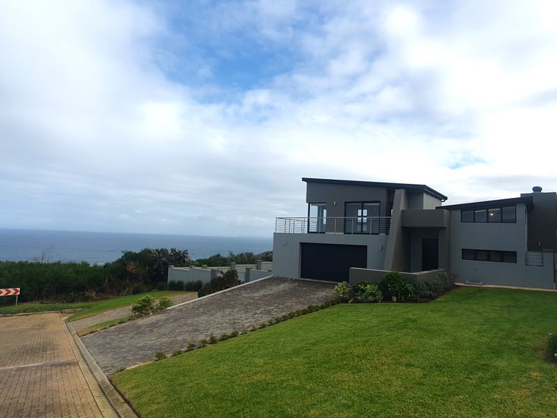 Modern multi-level coastal home featuring a paved driveway, integrated garage, and an elevated balcony with expansive ocean views.