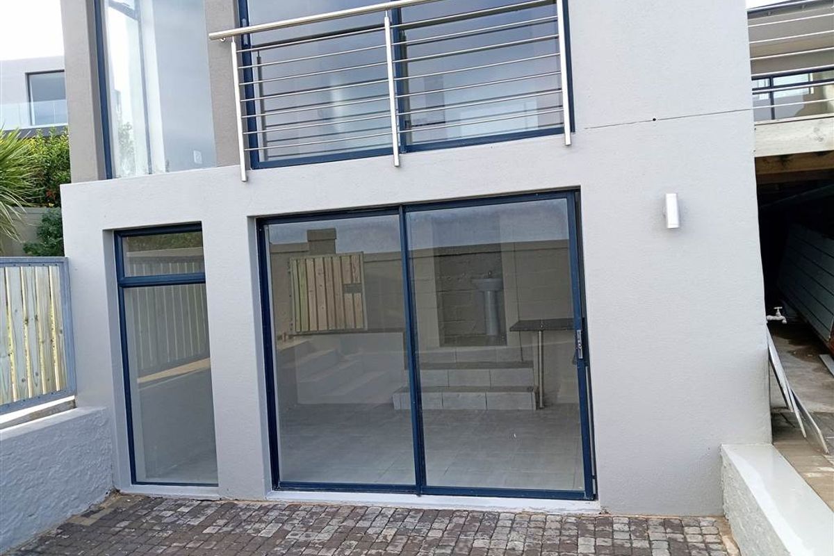Modern exterior view featuring a paved patio area, sliding glass doors, and a stainless steel balcony railing on the upper level.