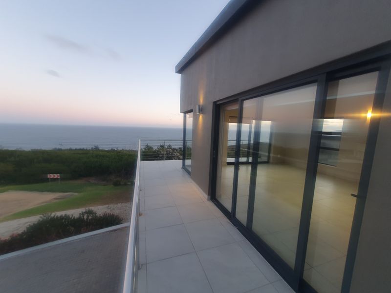 A spacious balcony with tiled flooring and stainless steel railings, offering expansive ocean views and direct access to the interior living space.