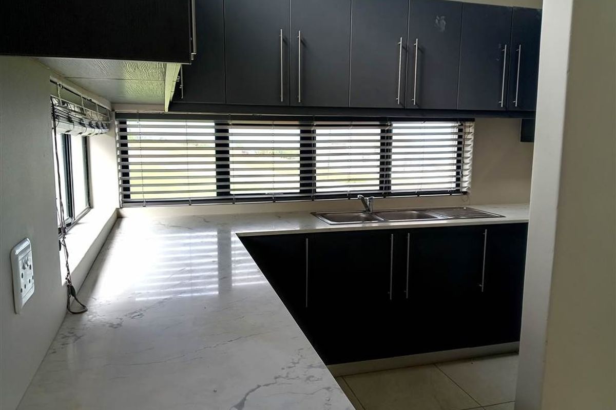 Modern kitchen featuring dark cabinetry, marble-look countertops, a double stainless steel sink, and horizontal window blinds.