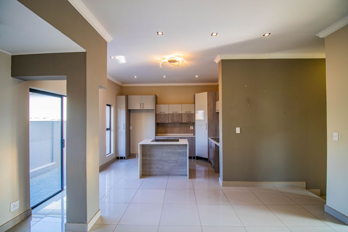 Modern open-plan kitchen featuring a central island with integrated hob, sleek cabinetry, and large format floor tiles, leading to an outdoor patio area.