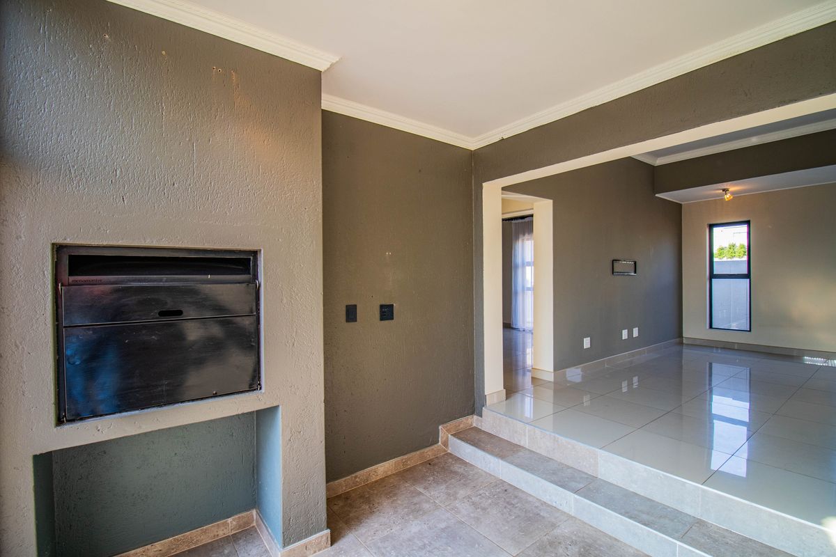 Spacious open-plan living area featuring a built-in fireplace, raised tiled flooring, and neutral wall tones, offering a versatile space for modern living.