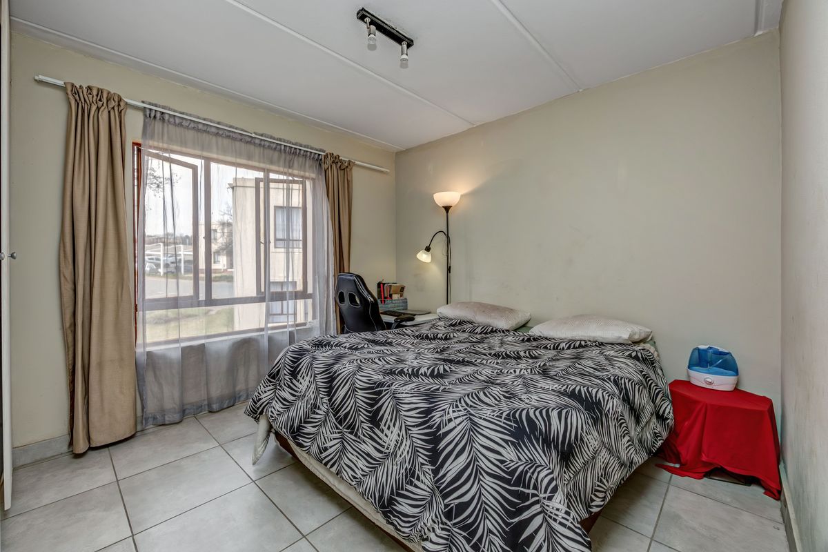 A functional bedroom featuring tiled flooring, a large window for natural light, and a standard ceiling-mounted light fixture.