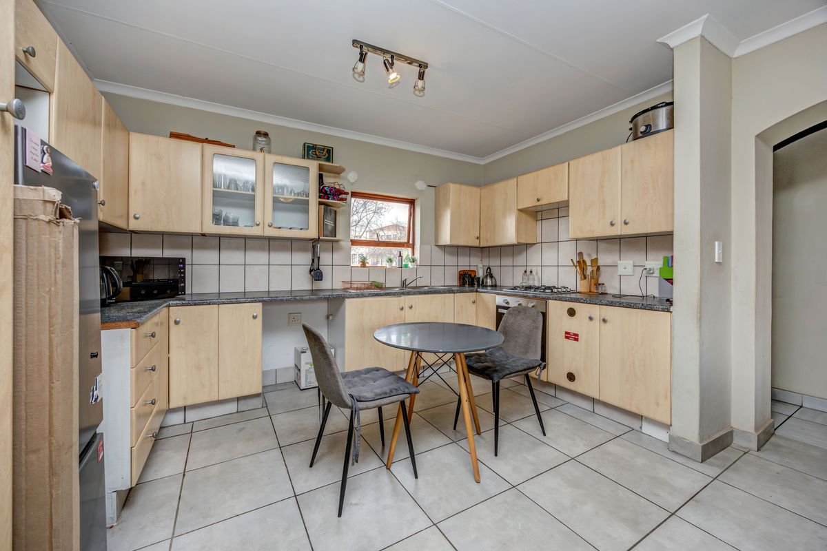 Functional kitchen featuring light wood-tone cabinetry, granite countertops, tiled backsplash, and integrated cooking appliances with space for a small dining table.