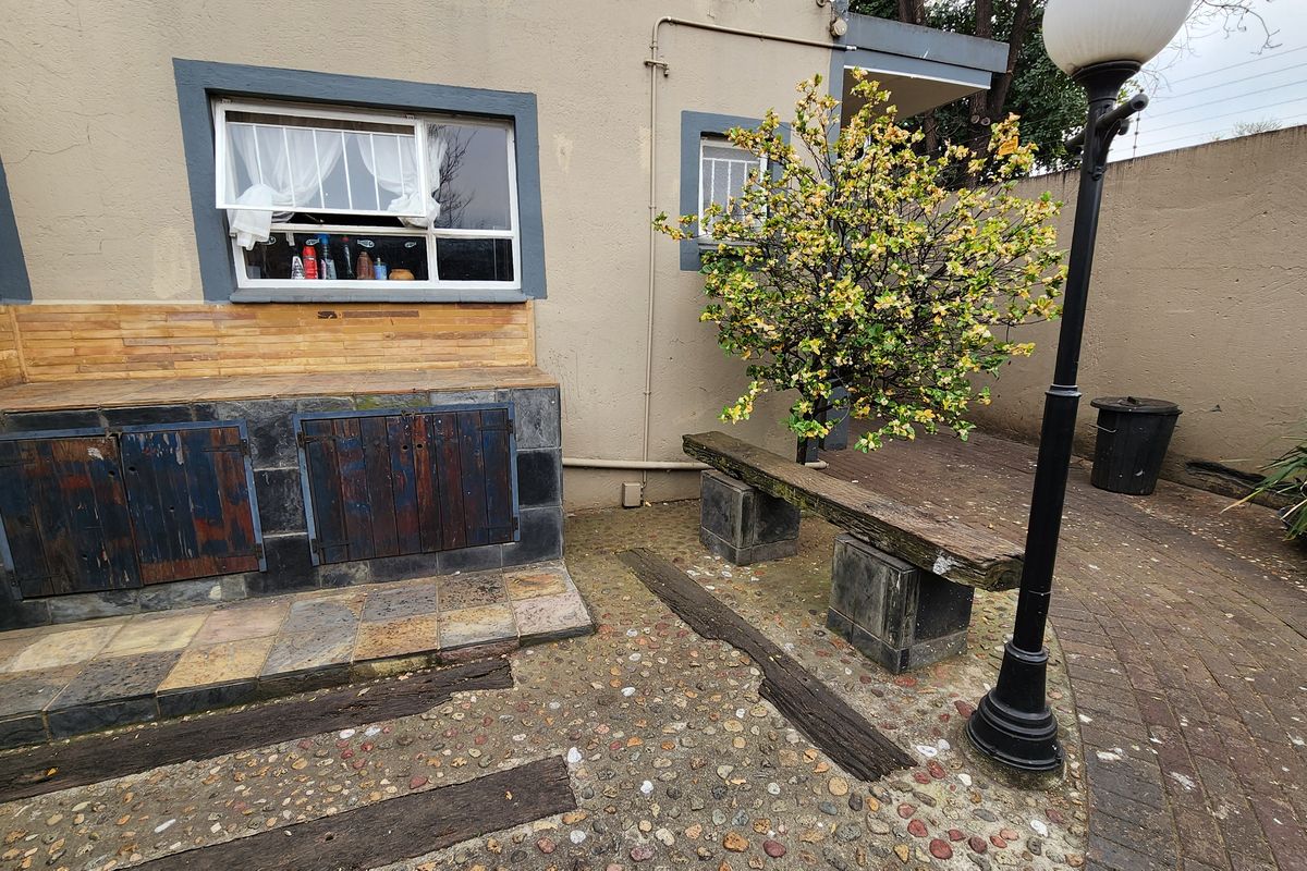 Rear courtyard area featuring a built-in braai station, stone paving, and a fixed garden lamp, offering potential for an outdoor entertainment space.