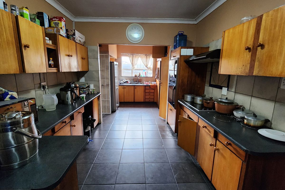 A functional kitchen featuring wooden cabinetry, dark laminate countertops, and tiled flooring, offering a practical layout with a separate scullery area.