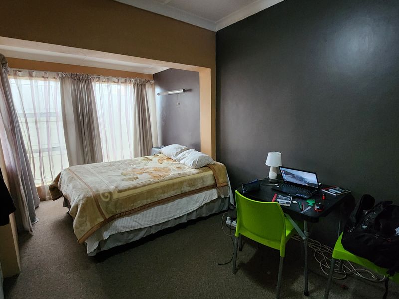 A bedroom featuring a recessed window alcove and carpeted flooring, providing a functional space with neutral and dark wall finishes.