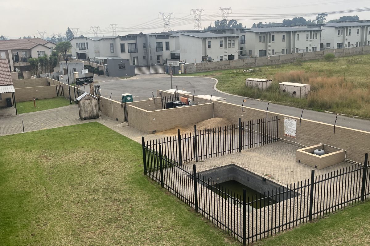 Aerial view of a townhouse complex featuring a communal swimming pool area, paved driveway, and perimeter security fencing.