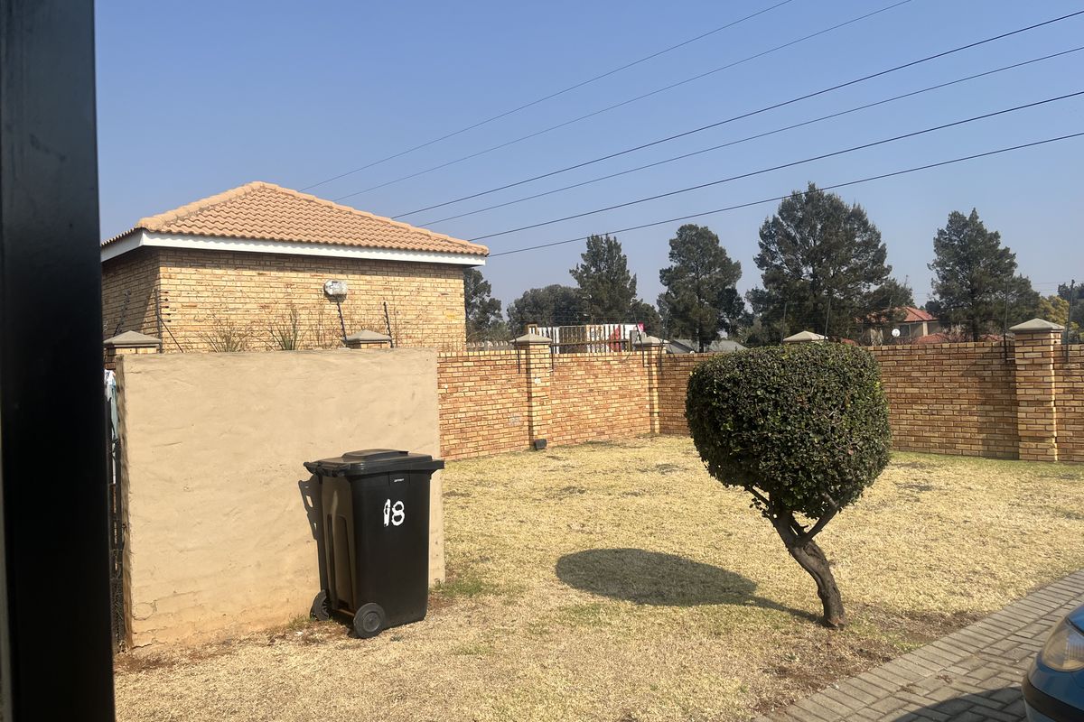 A rear exterior view of the townhouse featuring a brick boundary wall, paved driveway area, and a private garden space.