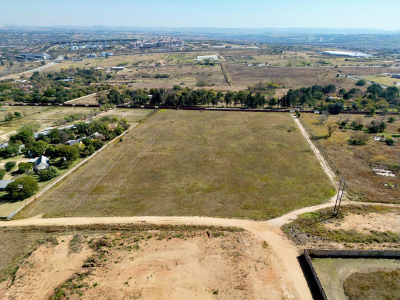 Aerial view of a large, vacant residential plot featuring perimeter walling and access via a dirt road in a developing area.