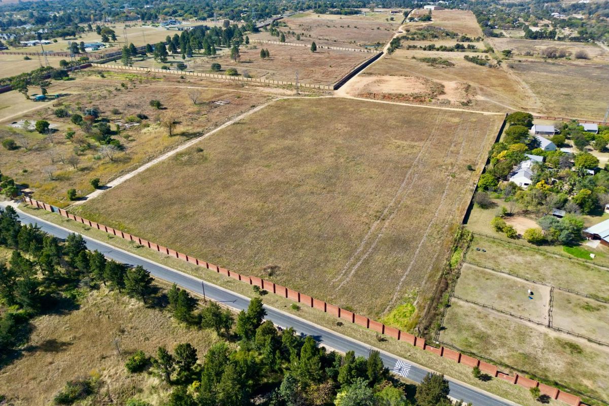 Aerial view of a large, vacant residential plot featuring perimeter walling and direct access to a paved road in a semi-rural setting.