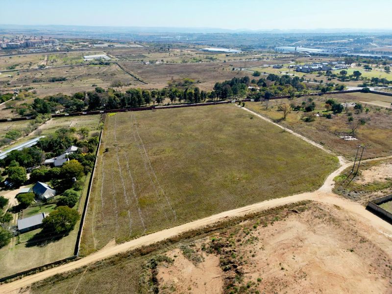 Aerial view of a large, vacant residential plot featuring open land, perimeter fencing, and access via an unpaved road in a developing area.
