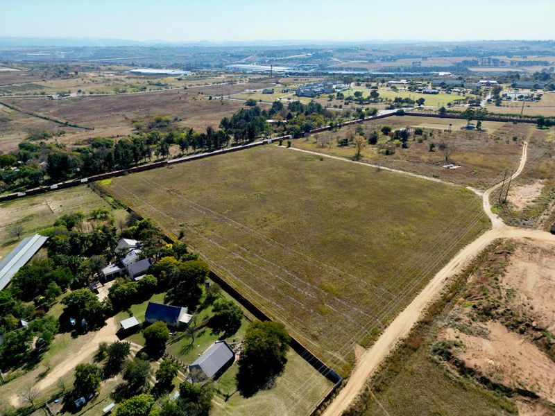 An aerial view of a large, vacant residential plot featuring perimeter fencing, adjacent dirt access roads, and surrounding rural landscape.