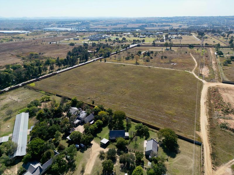Aerial view of a large vacant residential land parcel featuring established trees, existing outbuildings, and perimeter fencing with access road frontage.