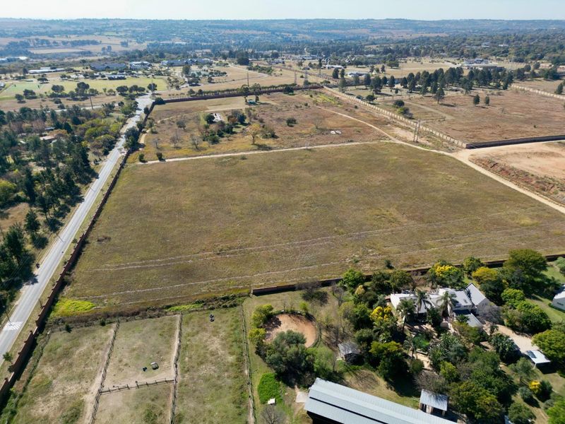 An aerial view of a large, vacant residential plot featuring open land, perimeter fencing, and proximity to local infrastructure.