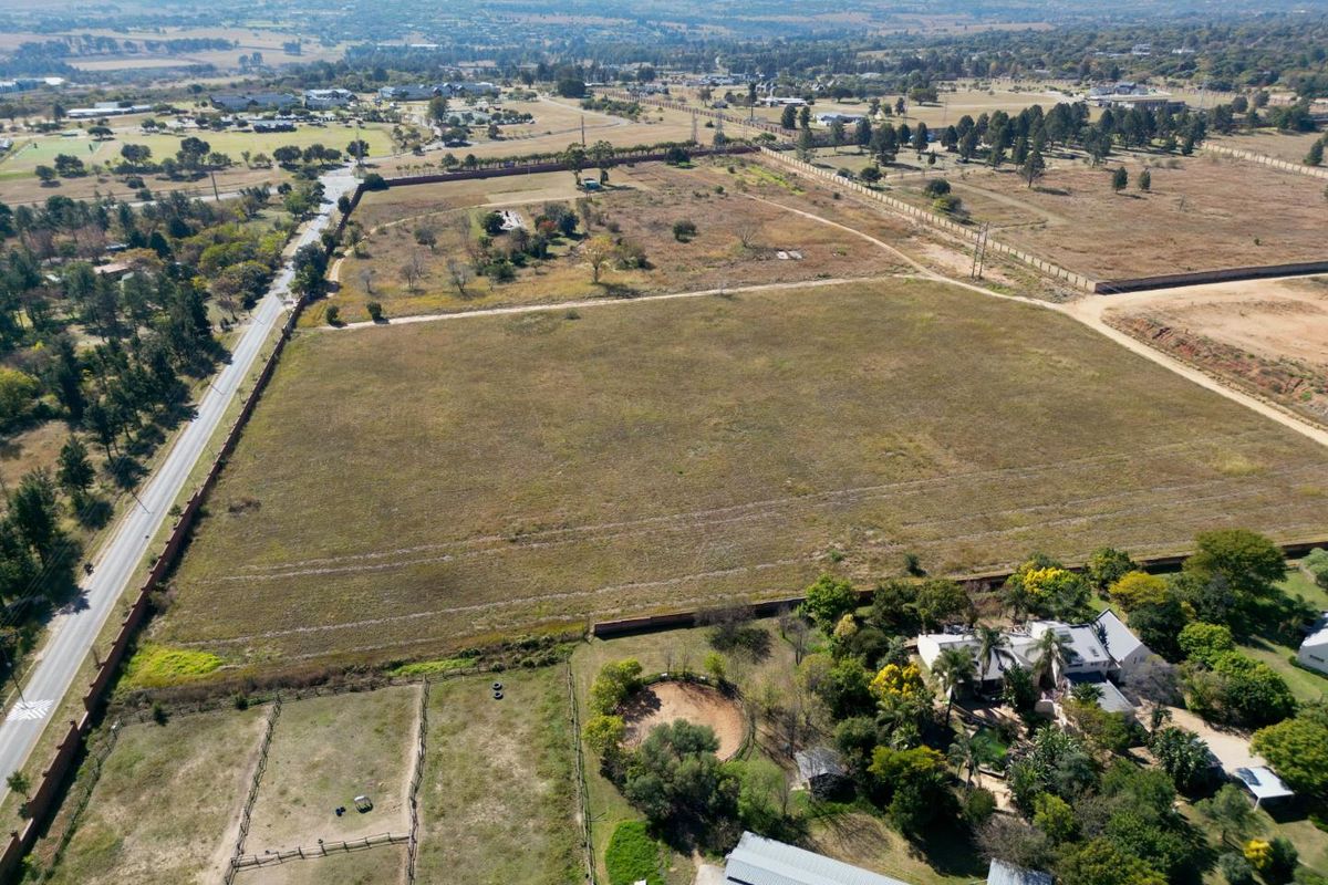 An aerial view of a large, vacant residential plot featuring open land, perimeter fencing, and proximity to local infrastructure.