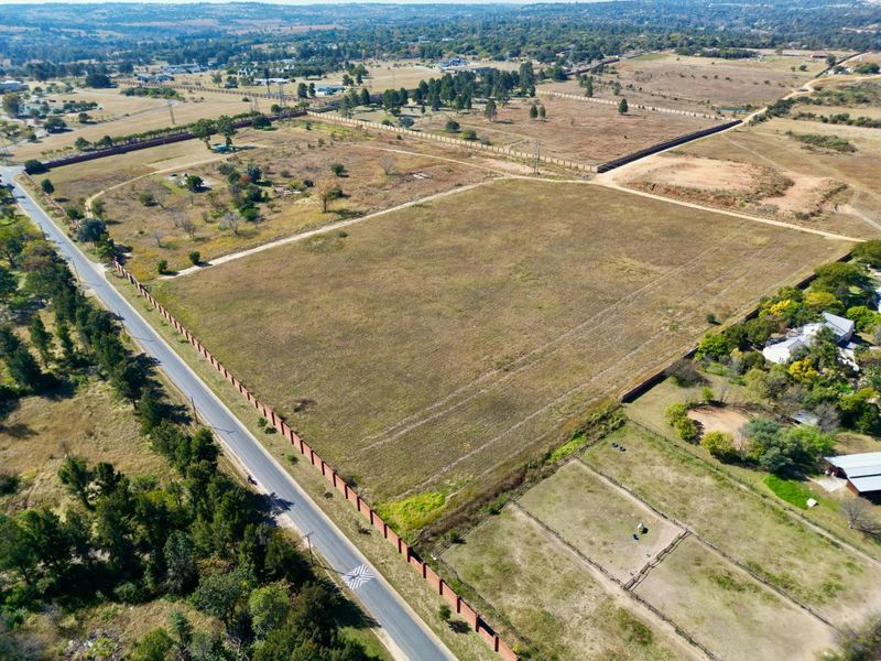Aerial view of a large, vacant residential land parcel with perimeter walling and direct access to a paved road in a semi-rural setting.