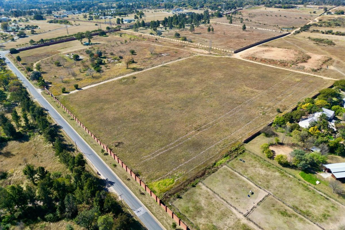 Aerial view of a large, vacant residential land parcel with perimeter walling and direct access to a paved road in a semi-rural setting.