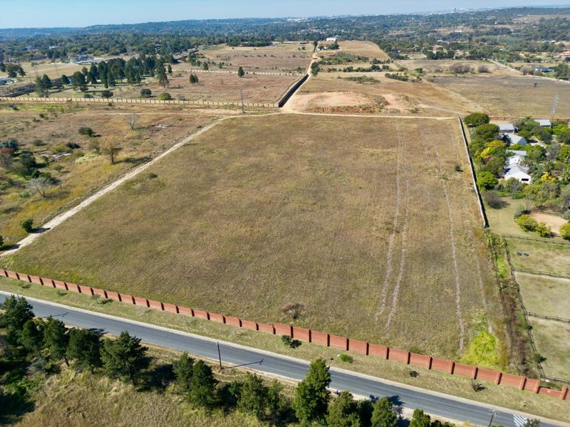 Aerial view of a large, vacant residential plot featuring perimeter brick walling and direct road access in a developing area.
