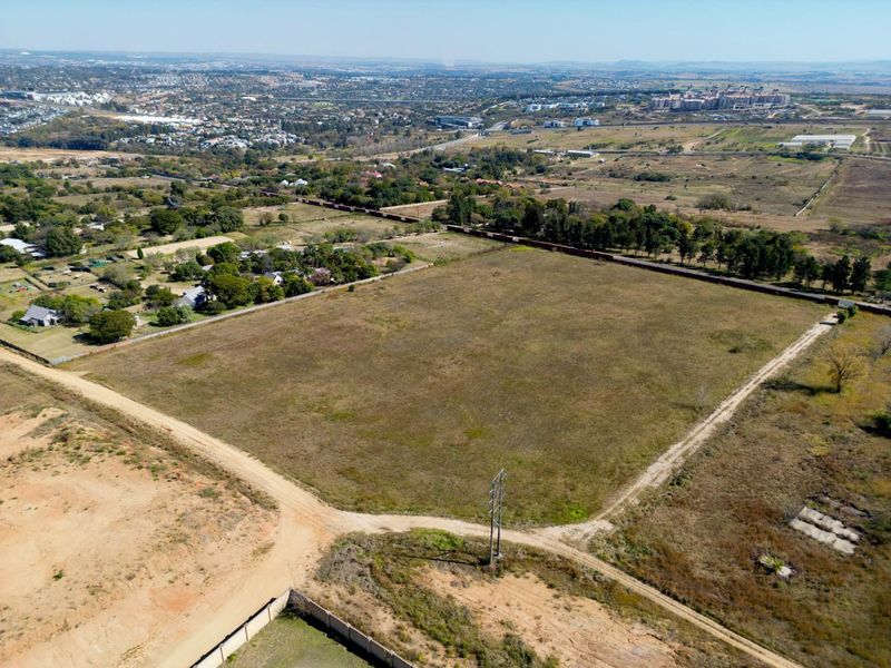 An aerial view of a large, vacant residential plot featuring established perimeter boundaries, access roads, and surrounding suburban landscape.