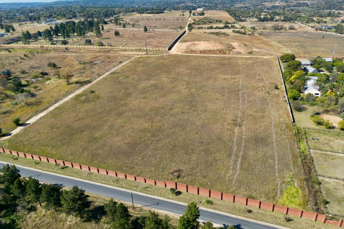 Aerial view of a large, vacant residential plot featuring perimeter brick walling and direct road access in a developing area.