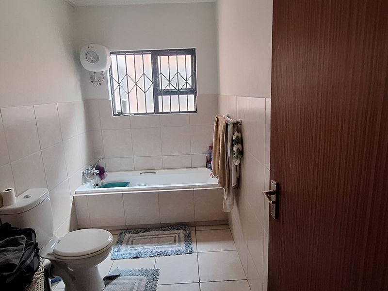 A functional bathroom featuring a bathtub, toilet, and tiled finishes, equipped with security bars on the window and an electric water heater.
