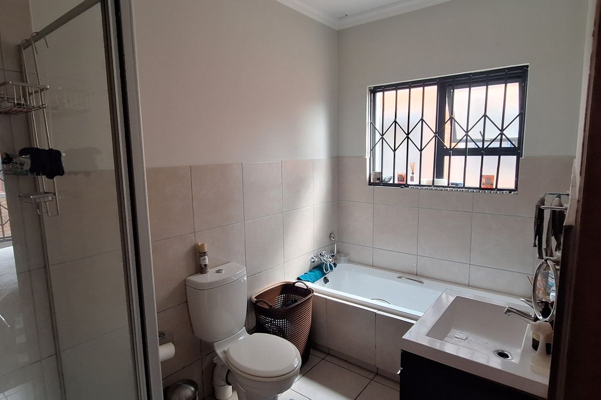 A functional bathroom featuring a shower enclosure, bathtub, vanity basin, and toilet, finished with neutral wall and floor tiles and security bars on windows.