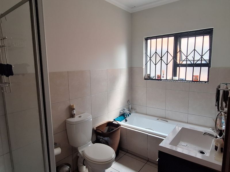 A functional bathroom featuring a shower enclosure, bathtub, vanity basin, and toilet, finished with neutral wall and floor tiles and security bars on windows.