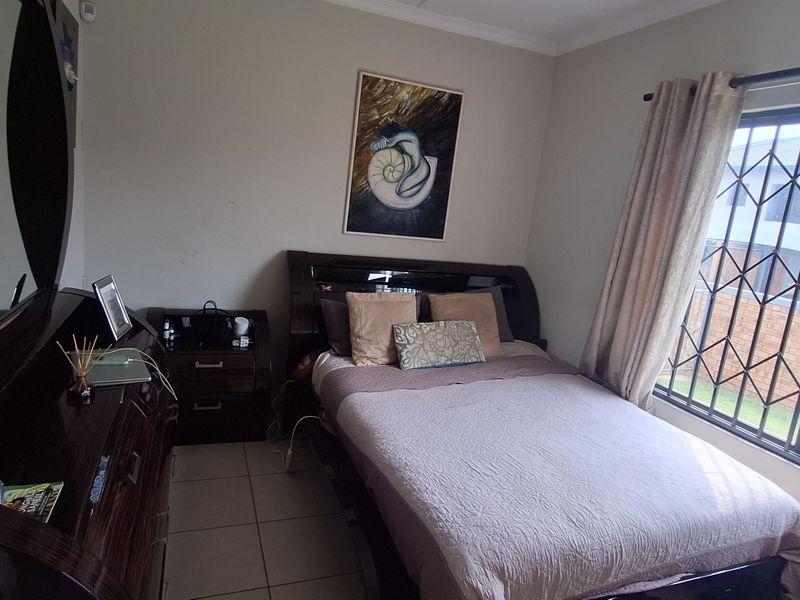 A functional bedroom featuring tiled flooring and a window fitted with a security gate, providing a secure and practical living space.