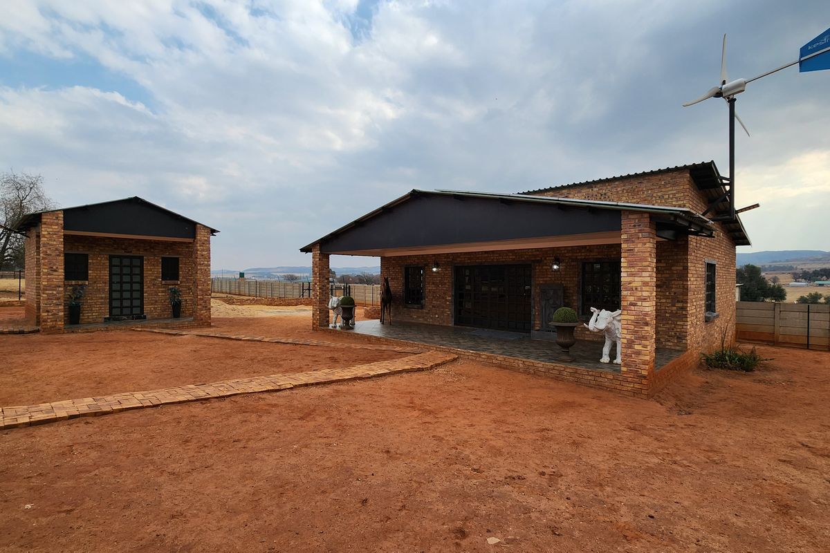 A view of the rear exterior featuring face brick construction, a covered patio area, and an installed wind turbine on a rural property.