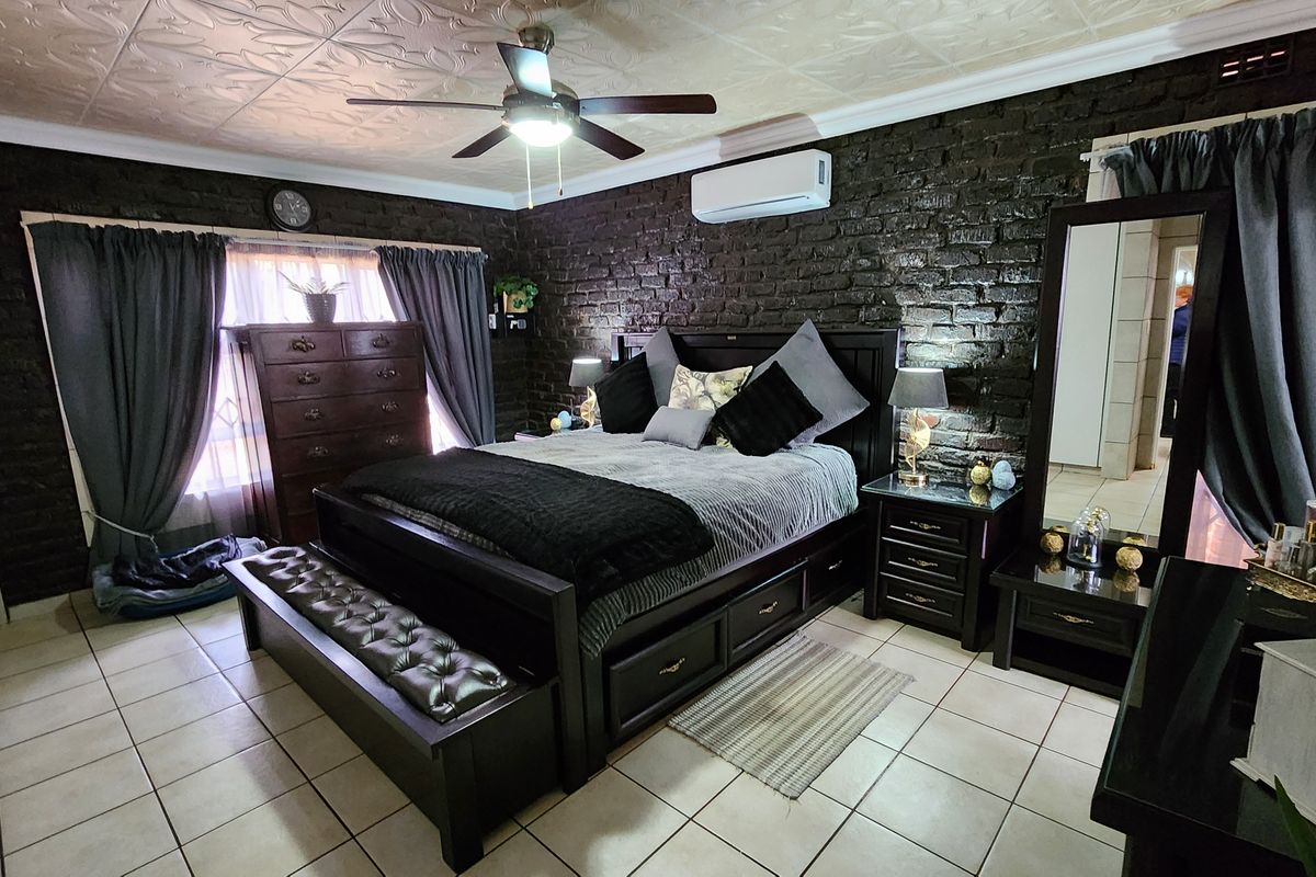 Spacious bedroom featuring a distinctive exposed brick feature wall, tiled flooring, decorative ceiling tiles, and a split-system air conditioner for climate control.