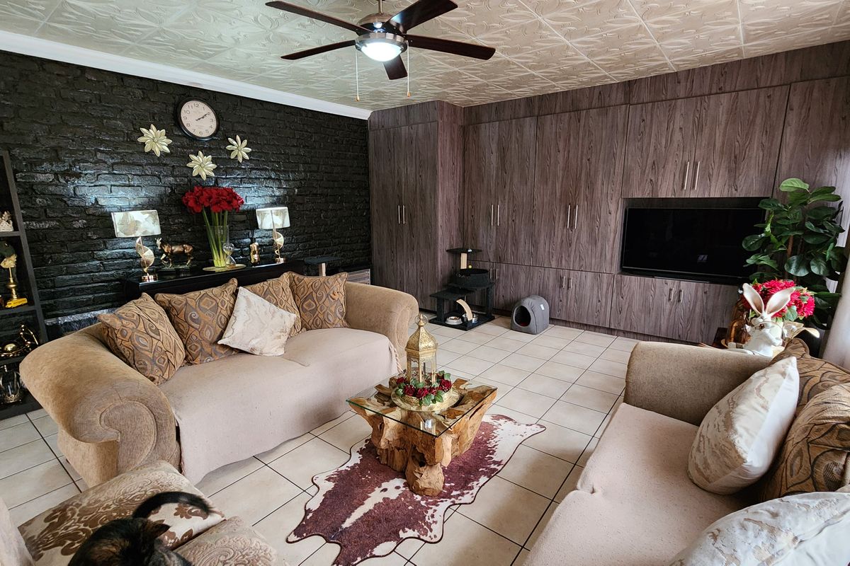 A living room featuring a dark exposed brick wall, extensive built-in cabinetry, tiled flooring, and a ceiling fan.