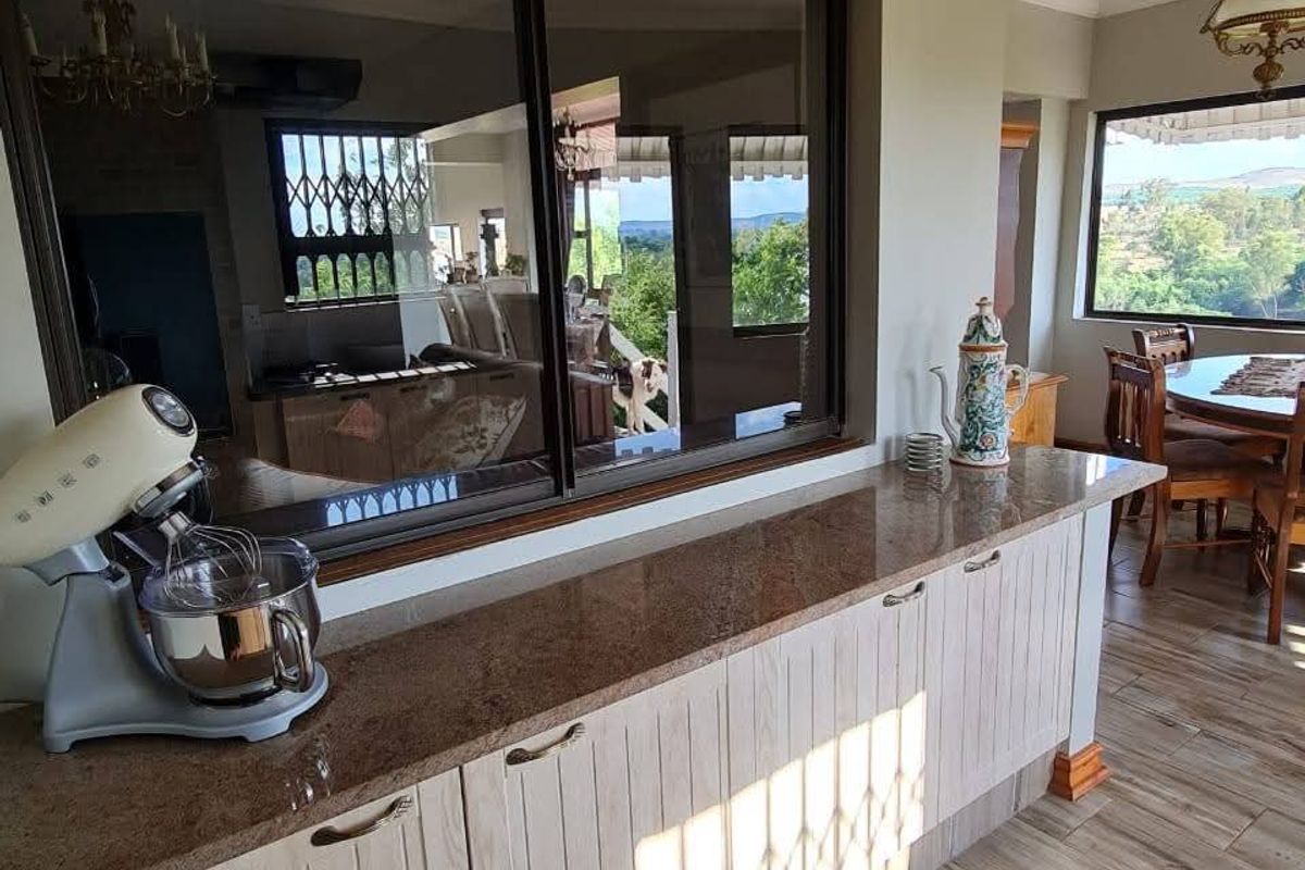 A bright kitchen area featuring granite countertops, light wood cabinetry, and large windows that provide natural light and views of the surrounding landscape.
