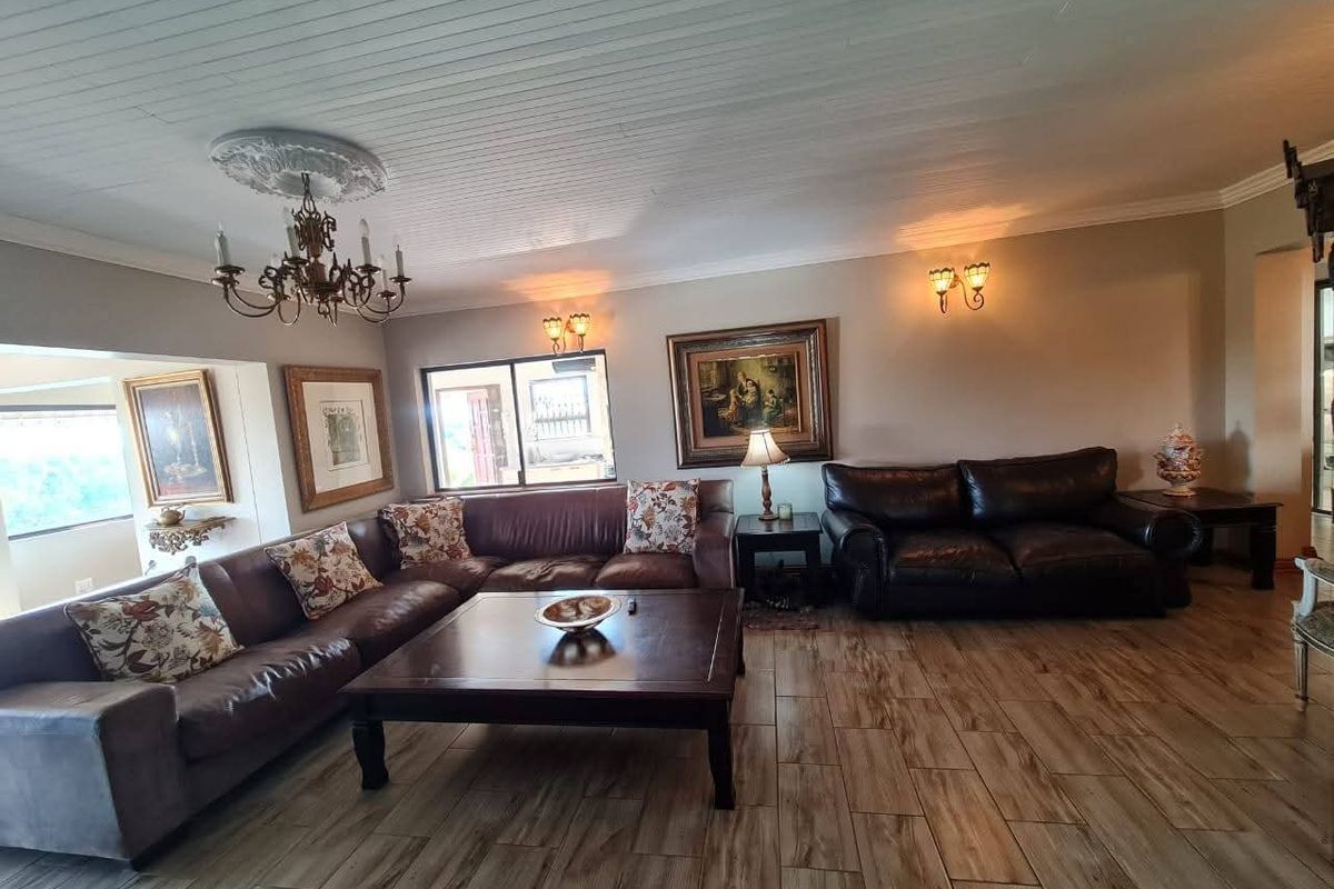 Spacious living room featuring wood-look tile flooring, a decorative ceiling medallion with chandelier, and wall-mounted sconce lighting.
